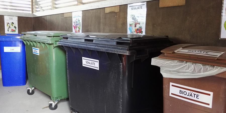 Kuva taloyhtiön jätekatoksesta, missä jäteastioita, joissa esimerkilliset lajitteluopasteet astiatarroineen.